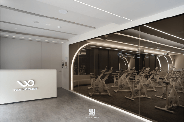 Wondercise健身房的接待區，白色櫃檯和光滑鏡面牆面，後方是運動區。